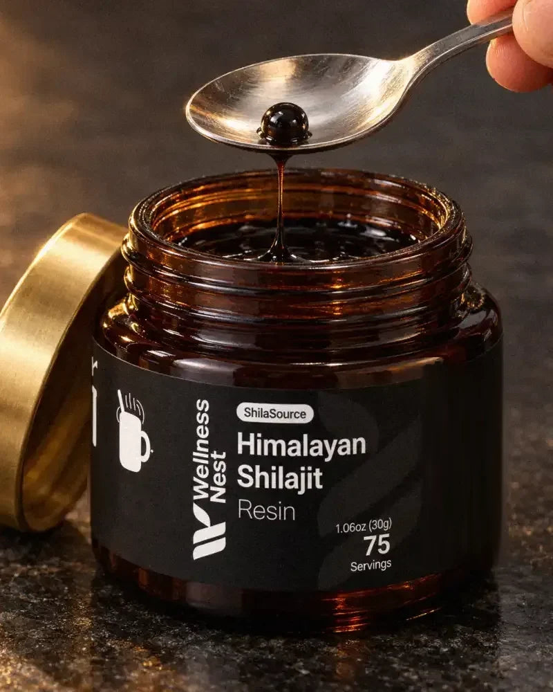 The open ShilaSource jar with its gold lid beside it and a steel teaspoon holding one pea-sized bead of black resin, a strand still joining it to the jar