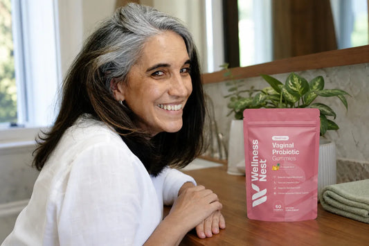 Woman in her early 60s at a bathroom vanity beside a pink Wellness Nest FloraFresh vaginal probiotic gummies pouch